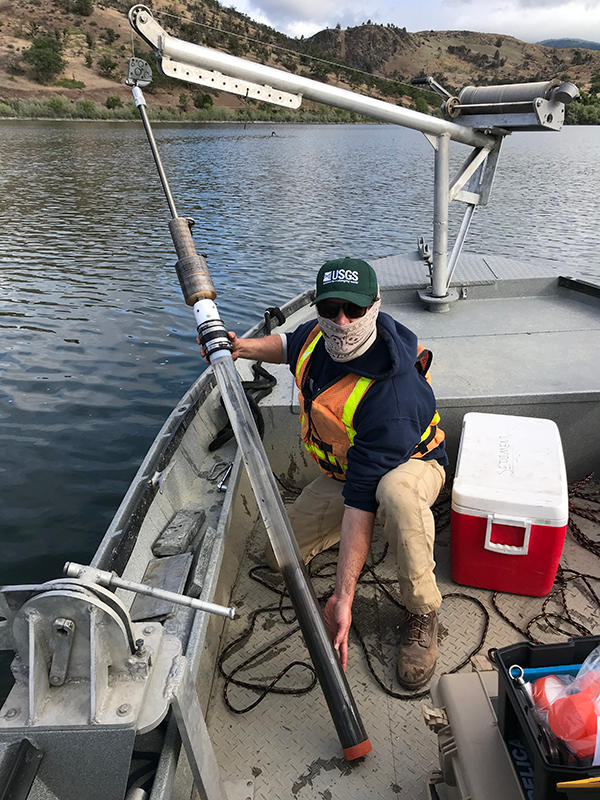 A scientist on a boat holds a long tube containing a sample of sediment and water.